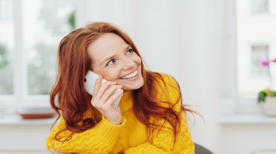A red-haired woman smiles as she talks on her cell phone